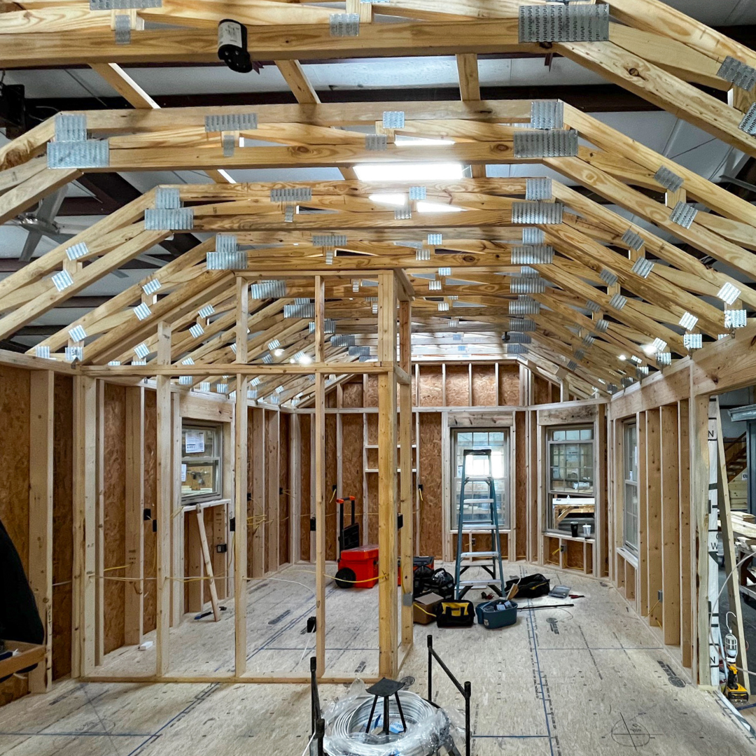 Social posts starting 7924 30 - Lelands Modular - Lelands Modular Interior of a framed house under construction with exposed roof trusses and metal plates, plywood floors, and scattered tools across the space.